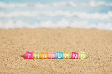 Word THAILAND from multicolored cubes in the sand on the background of beach and sea