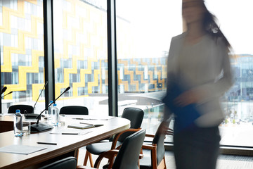 Background image of conference room in modern office with blurred shape of businesswoman walking to camera, copy space