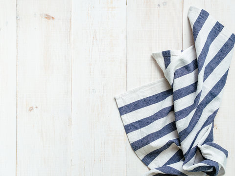 View From Above On White Wooden Table With Linen Kitchen Towel Or Textile Napkin. Blue Tablecloth On White Wood Tabletop. Copy Space For Text. Can Use As Mock Up For Design.