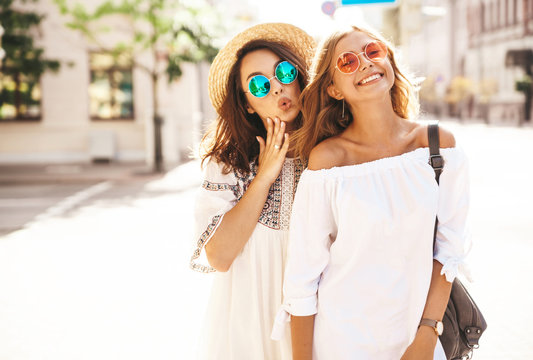 Fashion portrait of two young stylish hippie brunette and blond women models in summer sunny day in white hipster clothes posing on the street background. Going crazy