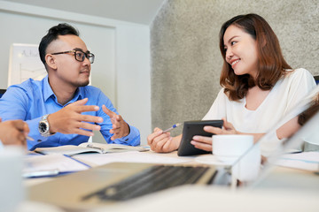 Obraz premium Young Asian man and woman with calculating machine working on report sitting at table with papers