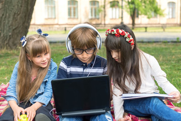 Three children study at the computer in the open air. Pupils, junior school sitting on the lawn....