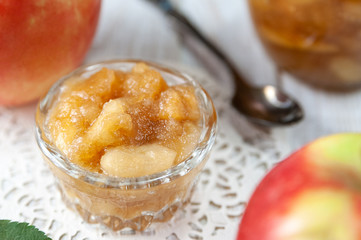 Small dish with apple jam with whole apples and a spoon on a white wooden table, selective focus