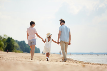 Fototapeta na wymiar Back view portrait of happy family holding hands while enjoying walk on beach during Summer vacation