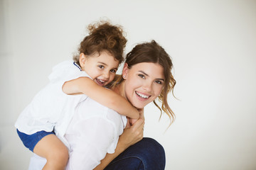 Young joyful mother holding little pretty daughter on back while