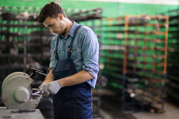 Young engineer in workwear standing by one of industrial machines and processing details