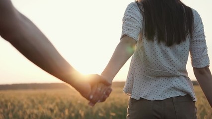 Loving couple spending time together in countryside, walking in field while sun going down, golden skies. Couple holding hands, connection.