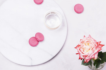 Before Breakfast. Empty glass and pink french cookies macaroons and rose flower on grey marble table and grey concrete background. Top view
