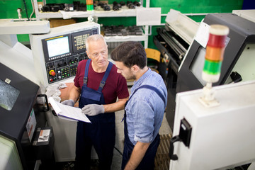 Senior engineer explaining to his younger colleague some information in document during working day