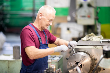 Senior grey-haired worker in uniform and gloves turning circle part of industrial machine