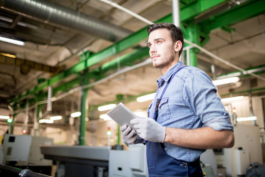 Young Serious Engineer In Workwear Holding Tablet While Searching For Online Information About Work Of Industrial Machines