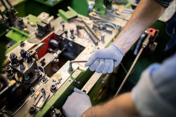 Gloved hands of modern factory engineer turning one of steel handles of processing machine