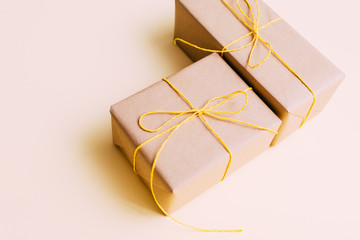 Gift boxes wrapped in brown kraft paper and tied with twine with beads and gold stars lie on a yellow background.Close-up.Design postcards for the holidays. Place for text