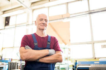 Cross-armed successful engineer in workwear and gloves looking at you in workshop