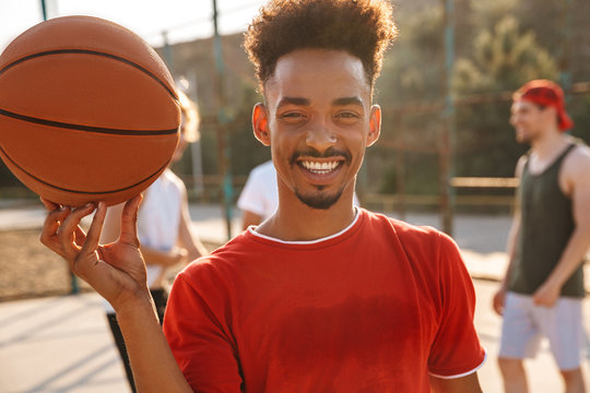 Portrait of american guy spinning ball on his finger, while playing basketball at the playground outdoor with his friends