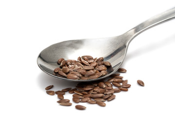 Close up of linseeds or flax seeds on a metal teaspoon isolated on white background