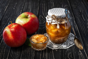 Small dish with jam and jar with apple jam with apples and a spoon on a black wooden table