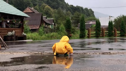 Little kid playing in puddles in yellow raincoat in the rainy day mobile footage