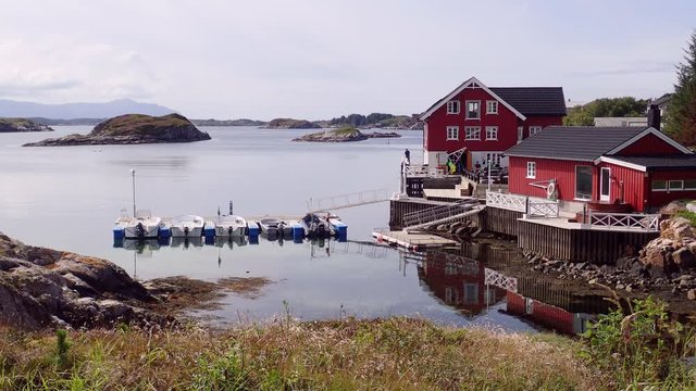 Red wooden house on the shore of the Norwegian fjord in sunny weather, Averoy, Norway
