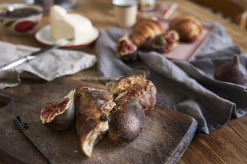 Breakfast with bread, croissants, figs, silver spoons on wooden rustic background, warm colors, close-up