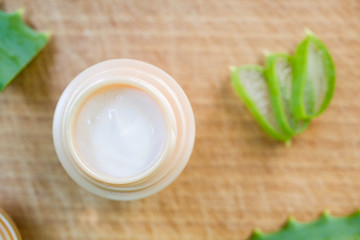 Green leaves of aloe vera plant and moisturizing cream on rustic wooden background
