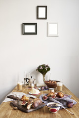 Breakfast in kitchen with photo frames on white wall. Croissants, figs, coffee, bread on wooden table background, empty space for layout