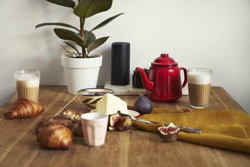 Breakfast with croissants, figs, coffee on wooden background, red tea pot, ceramics dishes, warm colors