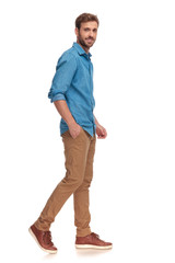 Naklejka premium smiling young casual man moving forward with hand in pocket