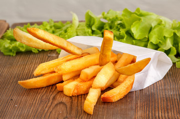 Delicate French fries on a wooden background.