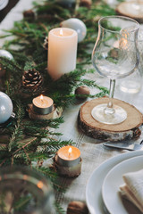 Festive Christmas and New Year table setting in scandinavian style with rustic handmade details in natural and white tones. Dining place decorated with pine cones, branches and candles