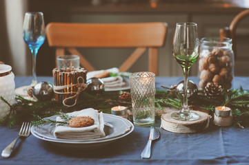 Festive Christmas and New Year table setting in scandinavian style with rustic handmade details in natural and white tones. Dining place decorated with pine cones, branches and candles