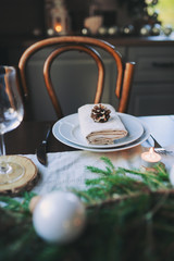 Festive Christmas and New Year table setting in scandinavian style with rustic handmade details in natural and white tones. Dining place decorated with pine cones, branches and candles