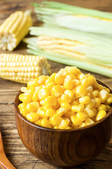 Canned corn in a wooden plate and cob of fresh corn on a rustic wooden background
