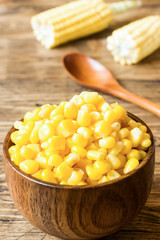 Canned corn in a wooden plate and cob of fresh corn on a rustic wooden background