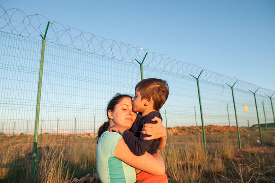 happy mother refugee reunited with child kissing her near fence barbed wire