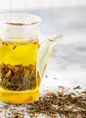 Green tea with strawberry flowers in teapot on gray table on light background