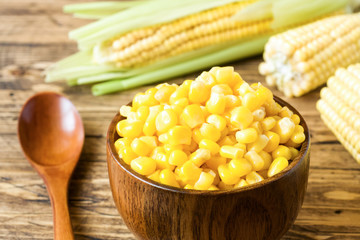 Canned corn in a wooden plate and cob of fresh corn on a rustic wooden background