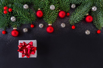 christmas gift on black background with fir tree branch and decoration, red berrys and baubles