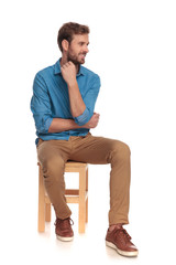 pensive young casual man looks to side while sitting