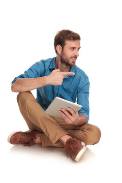 seated young casual man with tablet points to side