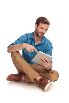 smiling seated casual man touching the screen of his tablet