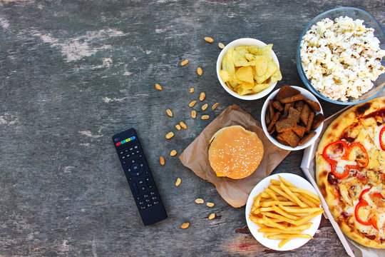 TV Remote Control, Fast Food On Old Wooden Background. Concept Of Junk Eating. Top View. Flat Lay.  .