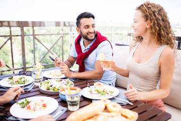 Portrait of modern Middle-Eastern man enjoying conversation with beautiful young woman while sitting at cafe table with friends, copy space