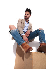 handsome man resting on wooden boxes looks down to side