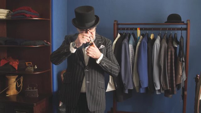 Portrait of posh chic virile millionaire or rich mature man visiting a luxury fashion boutique for buing new exclusive suit, lighting tobacco pipe