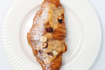Freshly baked croissant with nuts on a white plate
