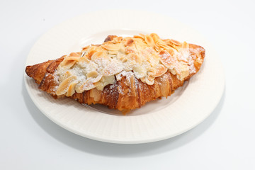 Freshly baked croissant with nuts on a white plate