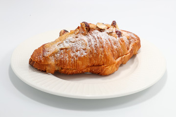 Freshly baked croissant with nuts on a white plate