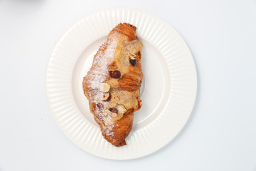 Freshly baked croissant with nuts on a white plate