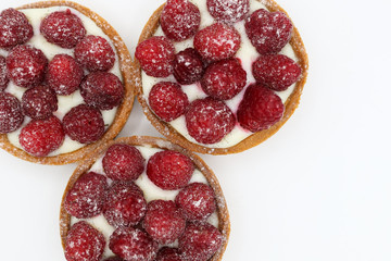 Three tartlets with raspberry on white background